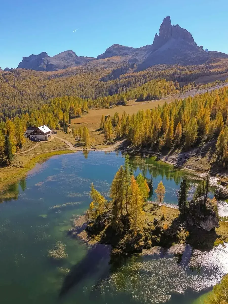 A mountain lake in the Italian Alps with a mountain hut, an island, towering mountain peaks and golden larches at Lago Federa