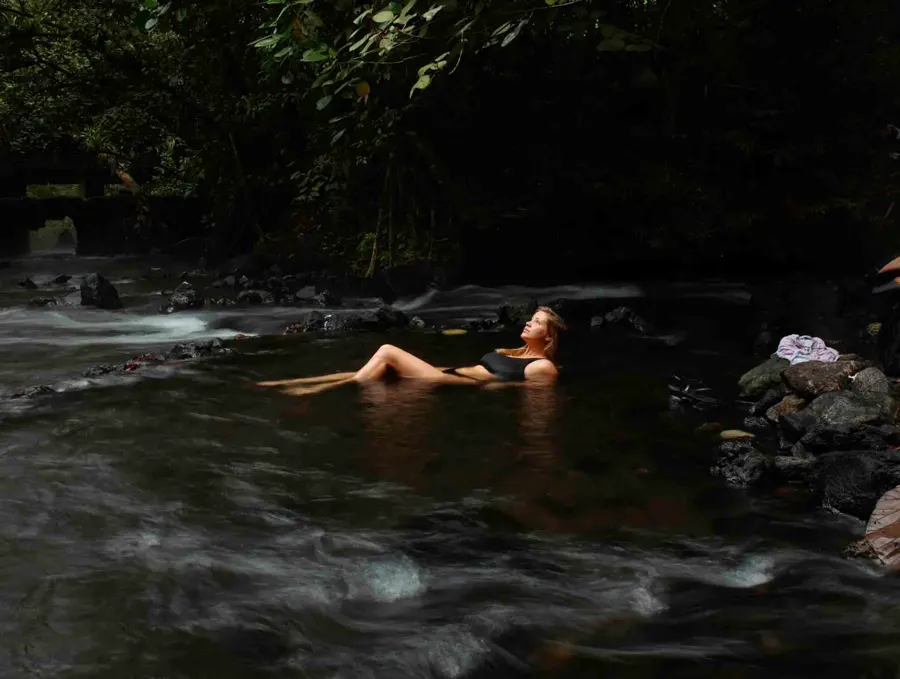 blonde woman laying in shallow hot springs the only free hot spring in La Fortuna in costa rica