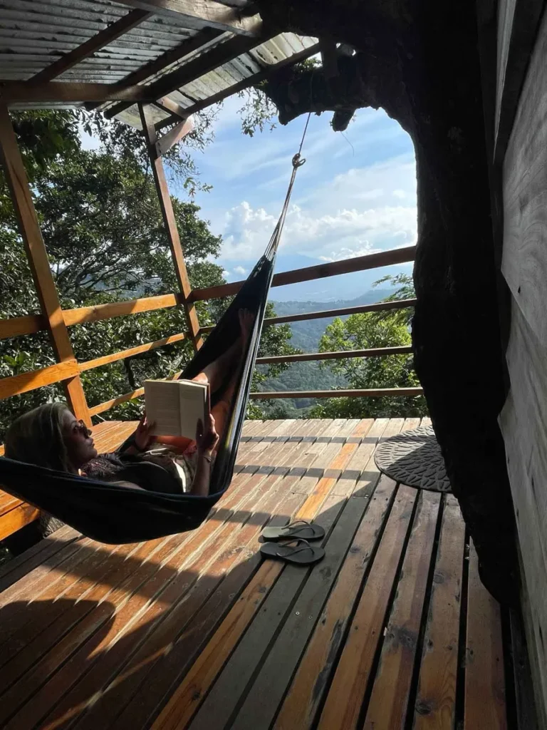 woman chilling in a hamock reading a book on a balcony at earth lodge in antigua guatemala with a view on jungle and volcanic landscape