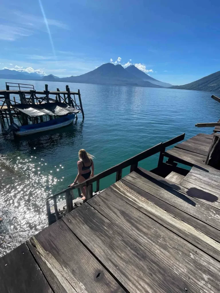woman walking down at the wooden dock at lake atitlan with views on the lake and surrounding mountains and volcanoes in guatemala