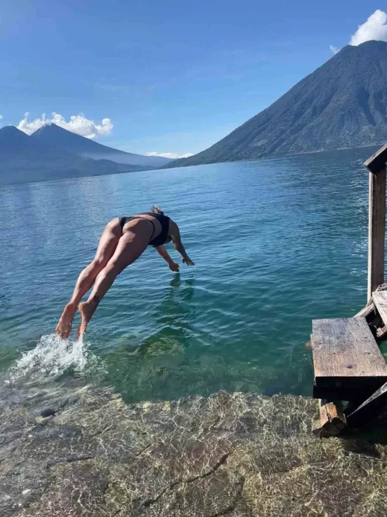 woman in a black bikini jumping in the lake atitlan at the dock at Pasaj Cap with views on the lake and the surrounding mountains and volcanoes in guatemala