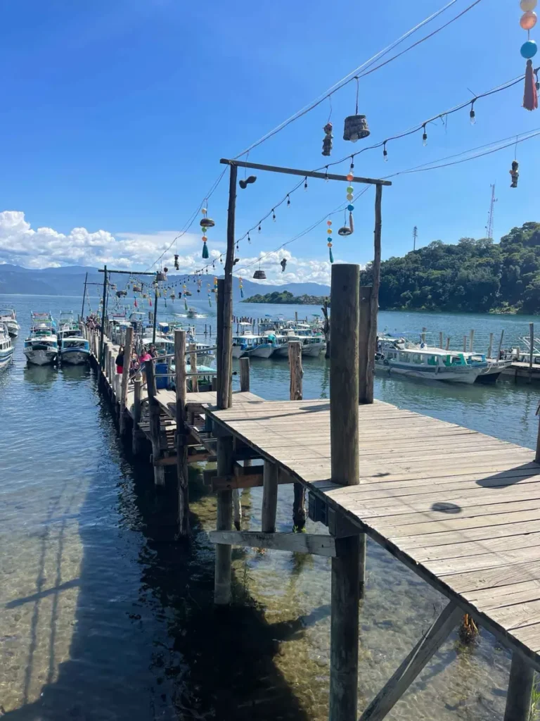 big wooden dock with multiple boats around at lake atitlan in guatemala with a view on the lake and surrounding mountains and volcanoes