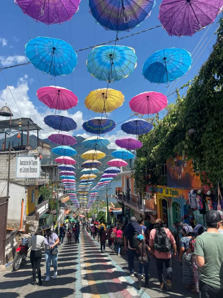 small art town San Juan La Laguna at lake atitlan with cobble stones, small houses, many tourists and colorful umbrellas hanging over the street with some views on the lake and volcanoes at lake atitlan in guatemala