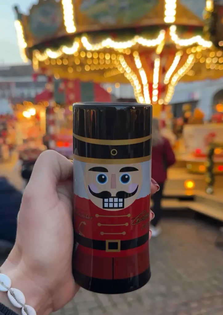 Hand holding a nutcracker Christmas mug in front of a carousel at the Christmas market in Saarbrücken