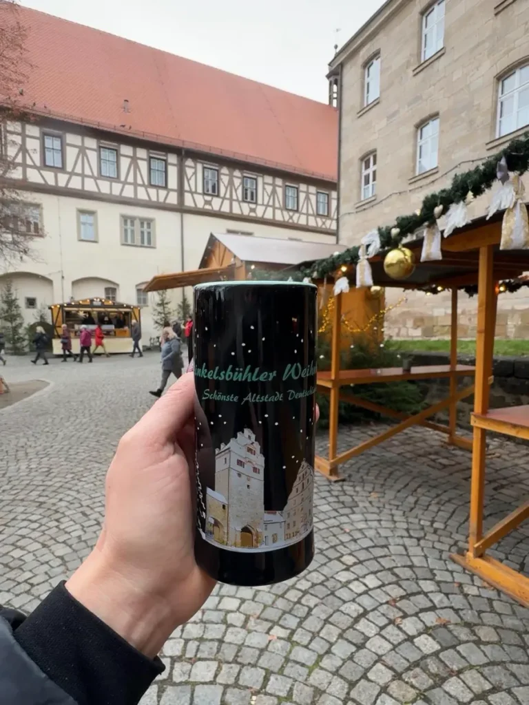 Hand holding a Christmas mug at a small Christmas market with some stalls, cobblestone roads and traditional houses in Dinkelsbühl