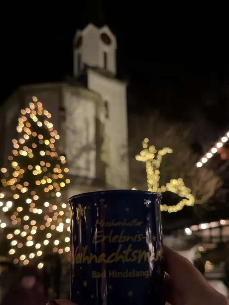 A hand holding a cup in front of a church at one of the most unique Christmas markets in Germany - Bad Hindelang
