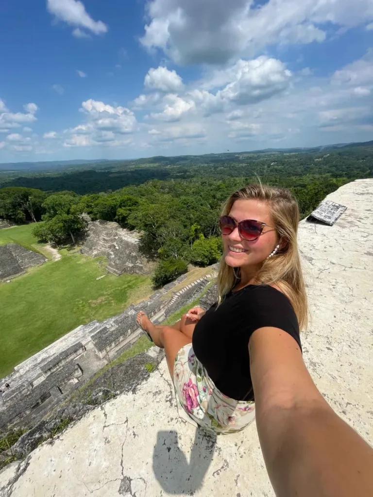 selfie from a blonde woman in a black outfit and sunglasses on top of the Xunantunich ruins with a view of surrounding grass and forest area