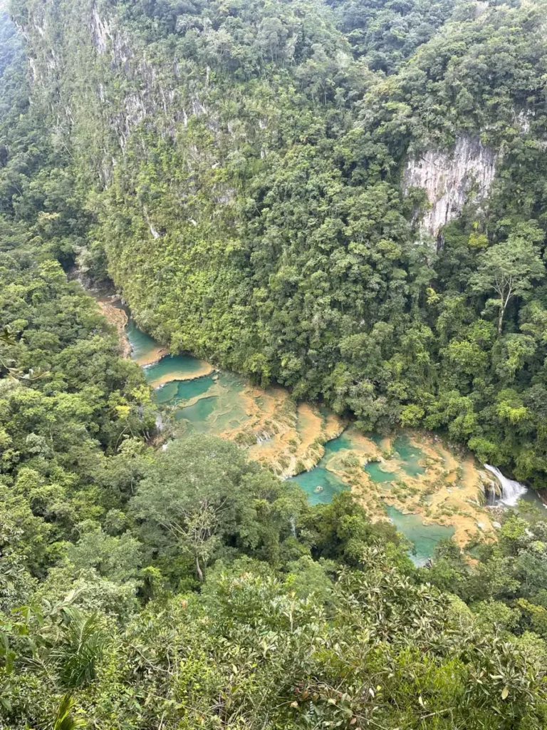 drone view over Semuc Champey a river forming multiple small waterfalls and pools with turquoise color with overgrown rocks in the middle of the jungle in guatemala