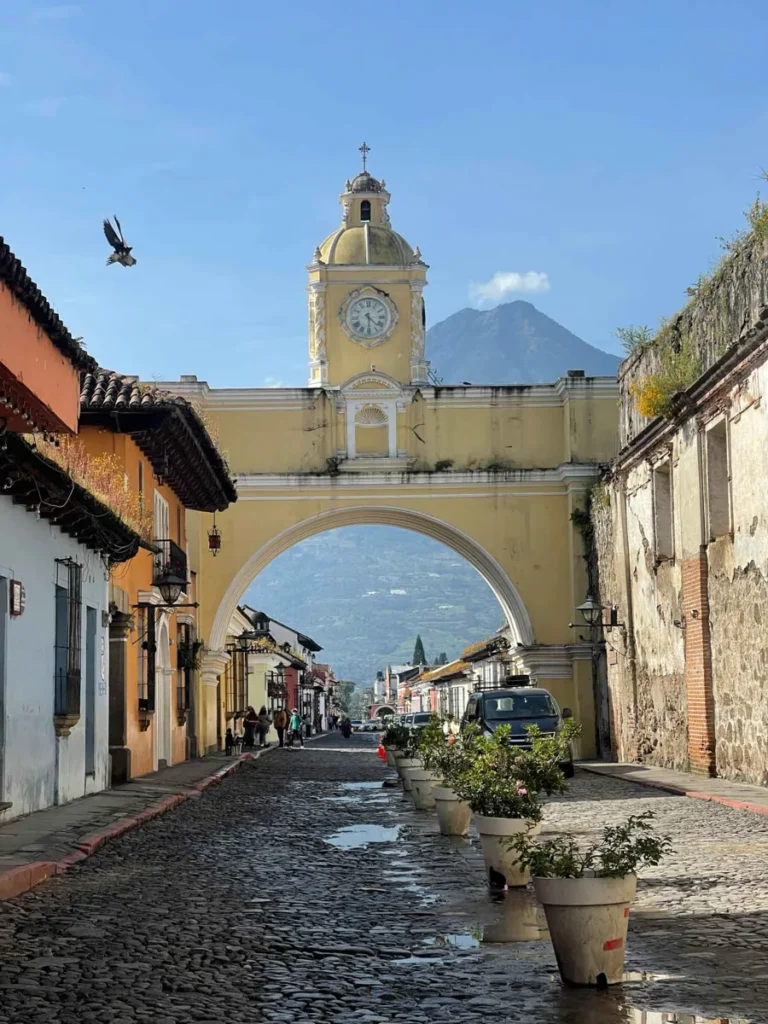 incredible things to do in Antigua, Guatemala colorful colonial street in antigua guatemala with cobble stones and an arch over the street with a volcano behind