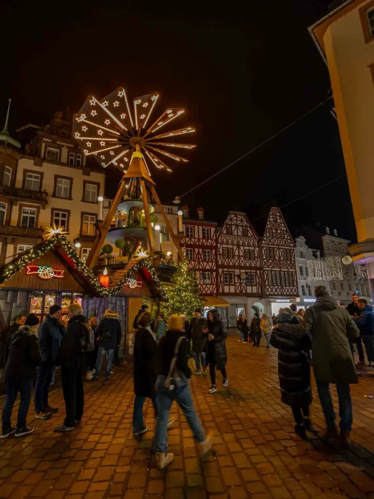 Christmas market stalls, people and a Christmas pyramid in front of historic houses in Trier, Germany