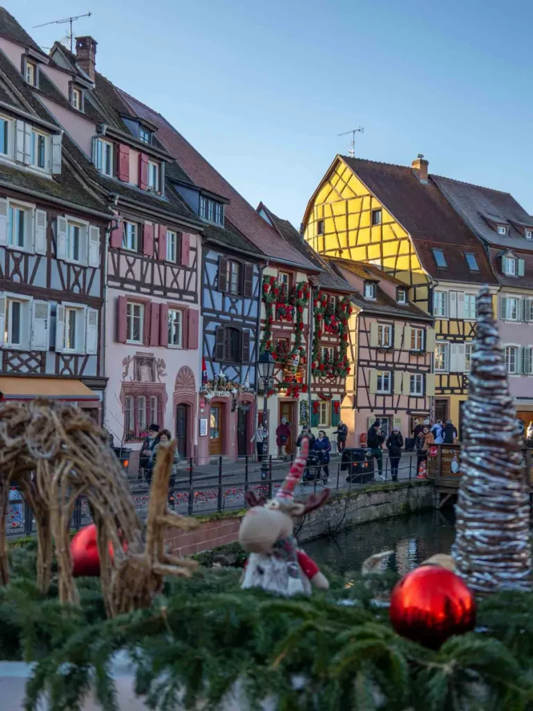 Colourful half-timbered houses along a canal with Christmas decorations and pedestrians in Colmar, France