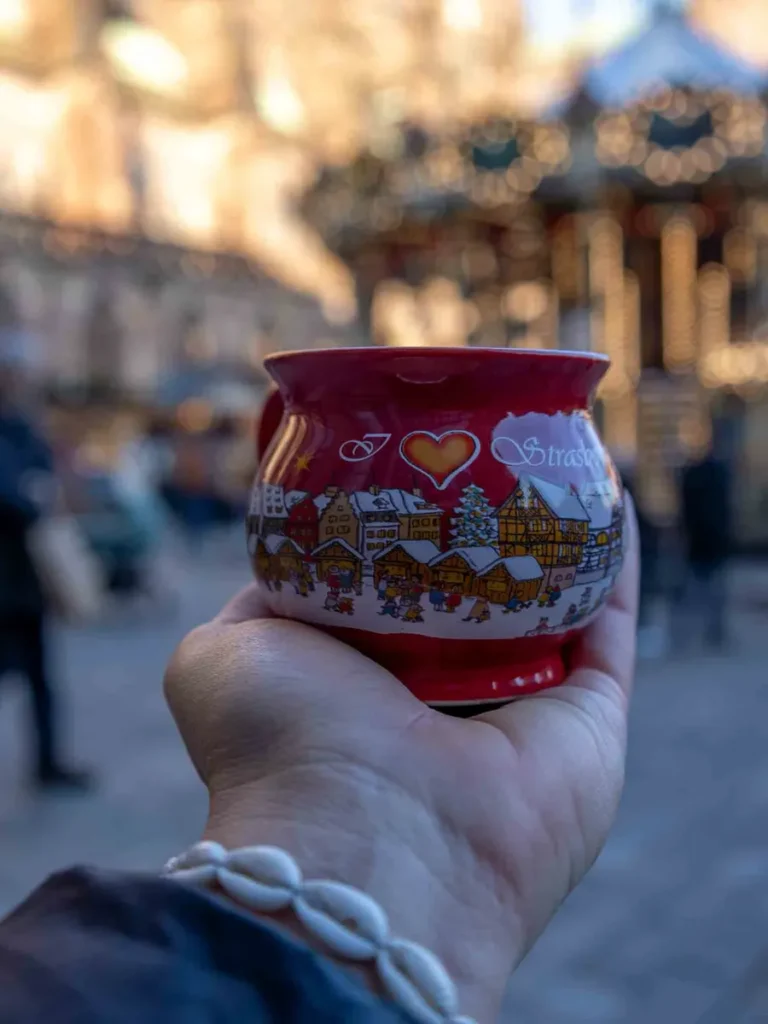 Hand with shell bracelet holding a Christmas cup on a Christmas market with a carousel in Strasbourg, France