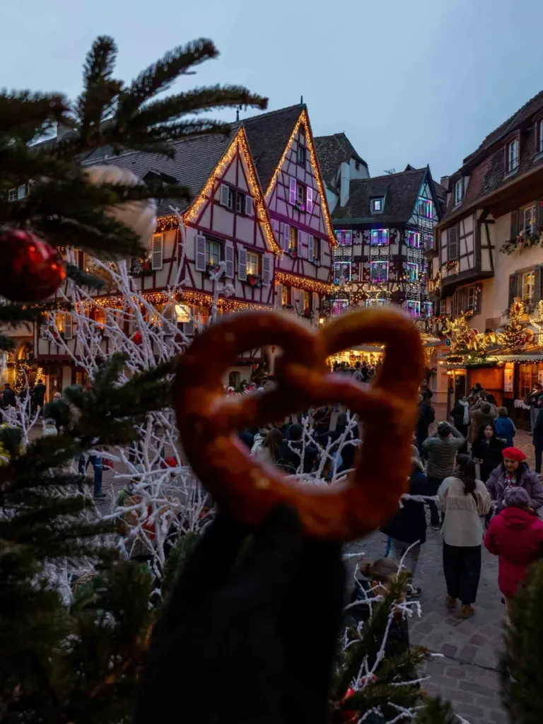 Hand holding a bretzel with festive houses in the background in Colmar, Alsace