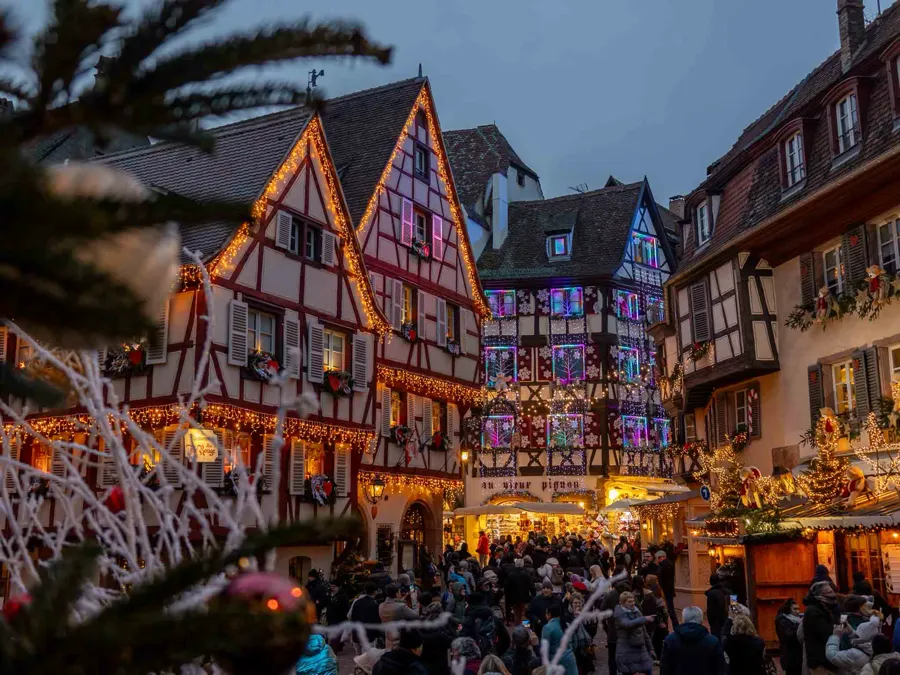 Half-timbered houses with christmas lights and decorations in Colmar, Alsace with many people on the streets