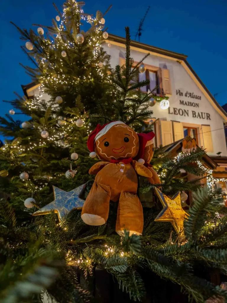 A christmas tree with Christmas lights and ornaments including a large gingerbread plush toy