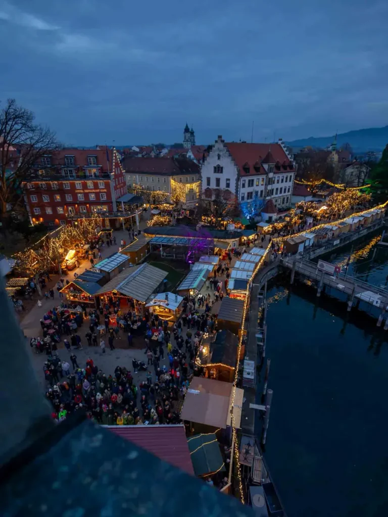 Bird's eye view of a Christmas market with stalls, people and traditional houses at the harbour of Lindau am Bodensee