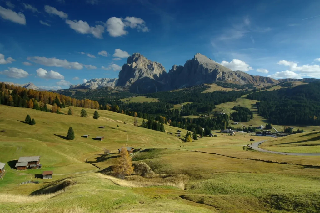 Bird's eye view of a stunning meadow in the Dolomites with golden rolling hills, mountain views and several huts at Alpe di Siusi